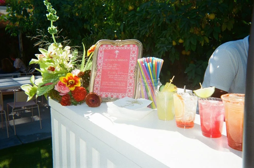Outdoor white bar decorated with flowers, greenery, and colorful cocktails