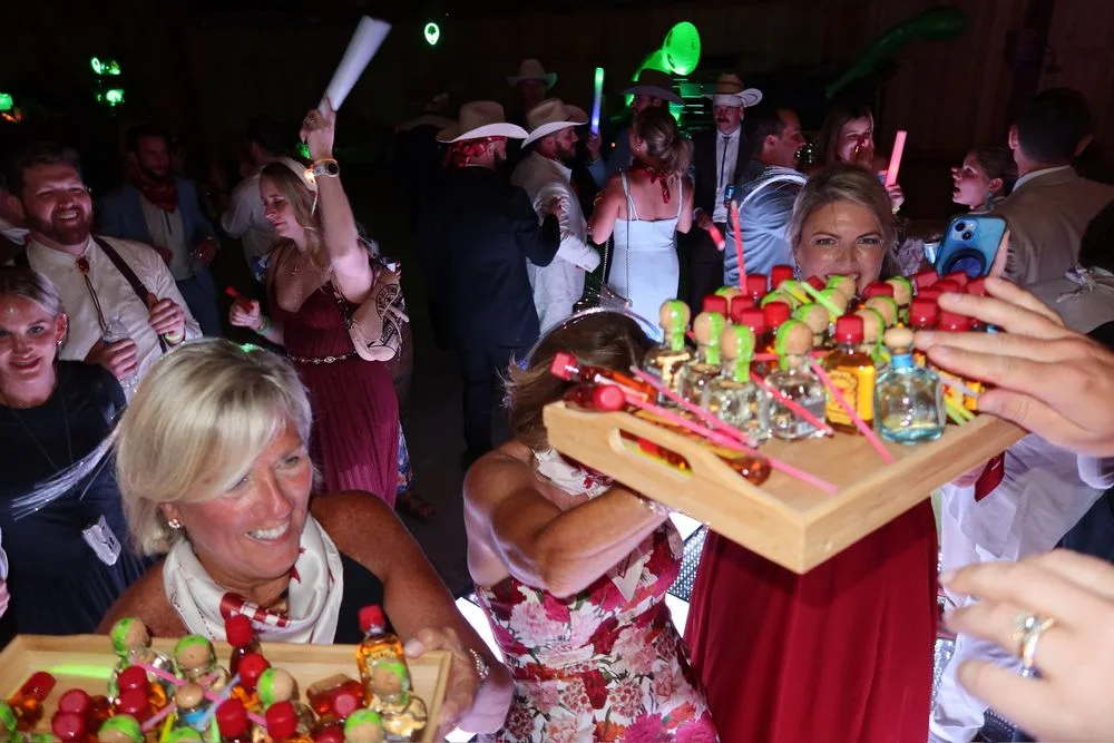 Wedding guests celebrating around a tray of colorful drinks at night